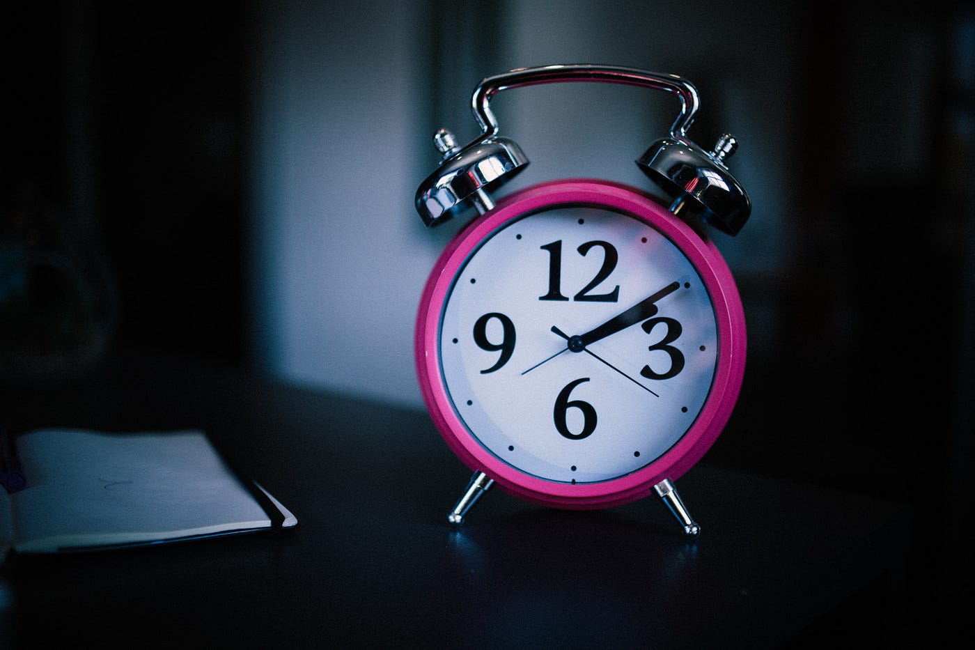 A traditional alarm clock (with a white face and pink rim) sits in a relatively dark room. The clock has two silver bells atop it. On average, the amount of deep sleep each study subject declined between the two studies, indicating slow-wave sleep loss due to aging.