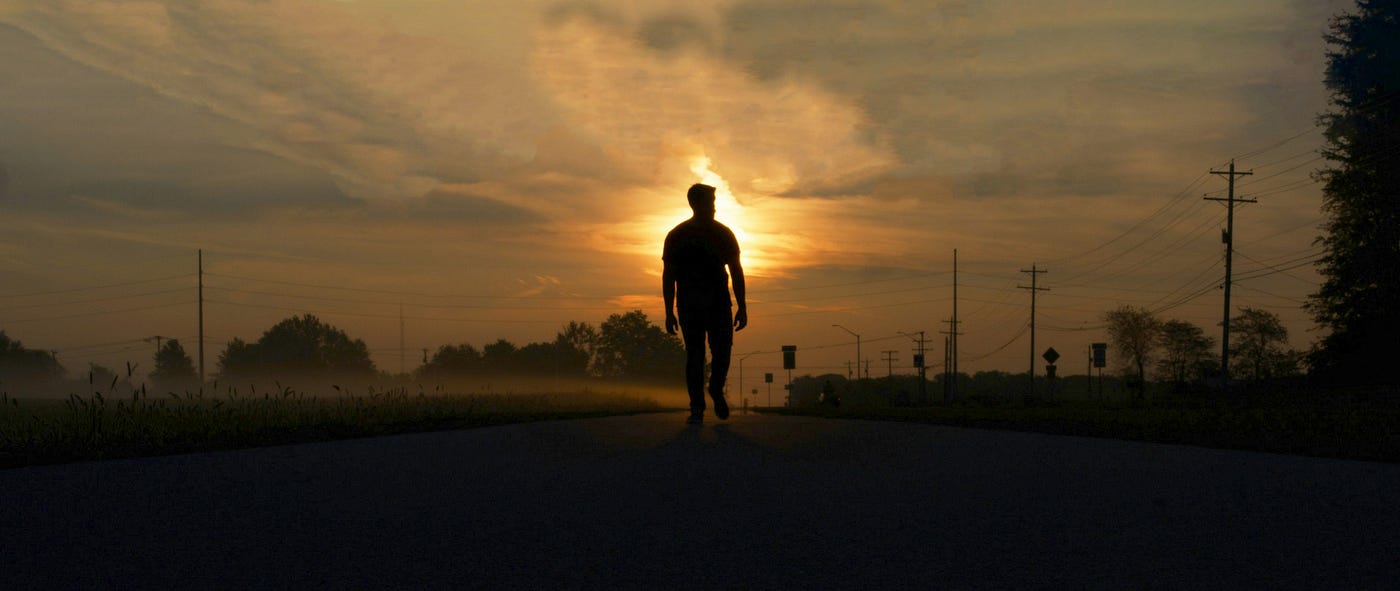 어둠에서 일출로 이어지는 길을 걷는 사람.