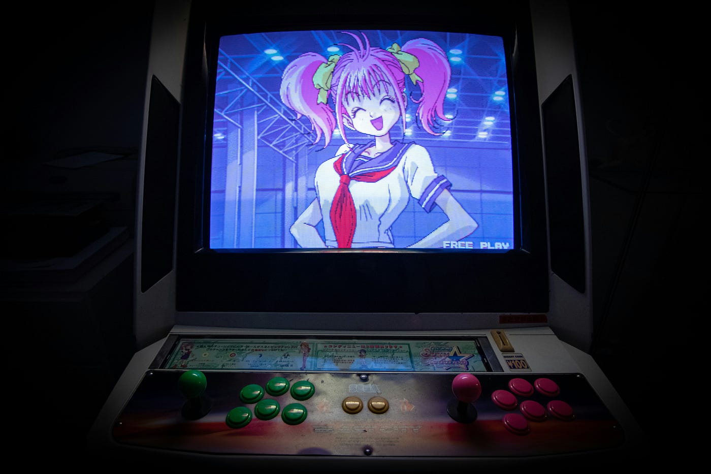 an old arcade with an anime girl on the screen. She has a big smile on her face