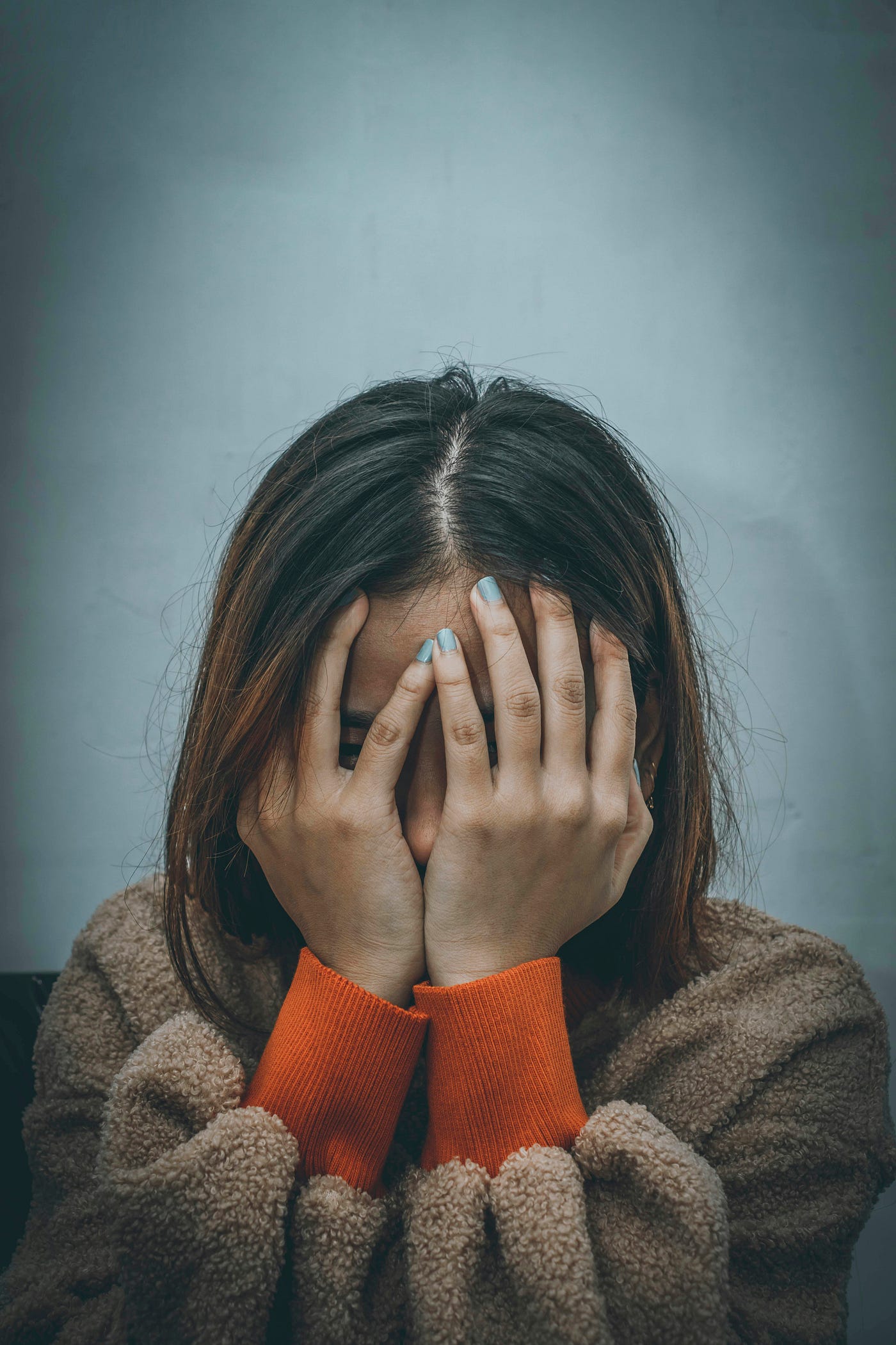 검은 머리의 여성이 얼굴 위에 손을 얹고 있다.<BR> 그녀의 손톱은 파랗게 칠해져 있다.<BR>