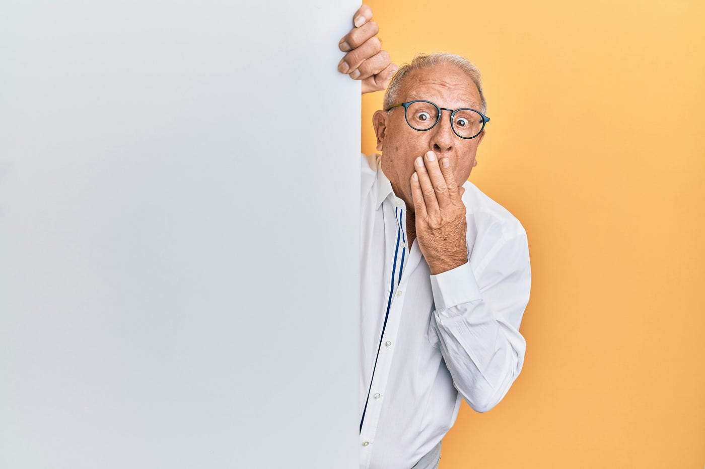 An older man in a white shirt expresses surprise by placing his left hand over his mouth.