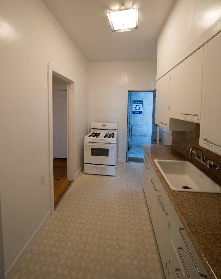 A small kitchen with the sink and cabinets on the right, and an oven farther back by a door to outside.
