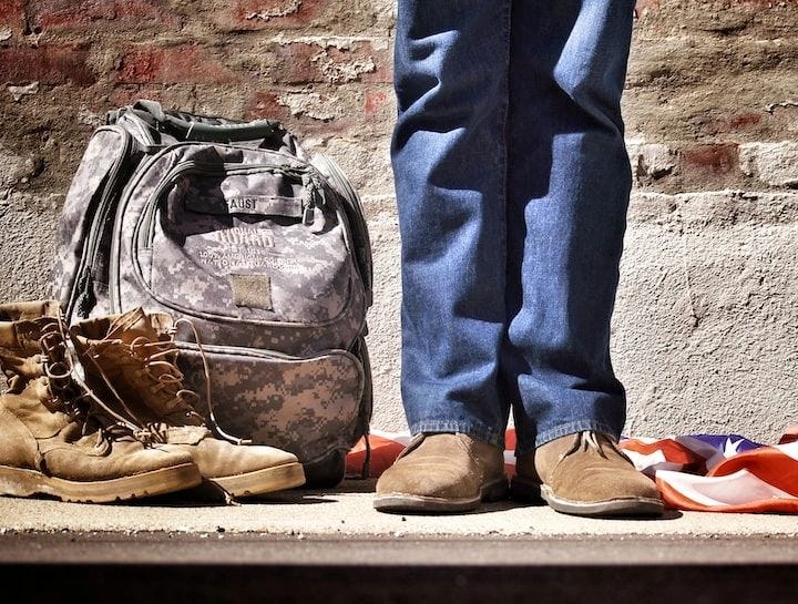 Mickey Markoff 2023 Air Sea Exec — photo of person in blue jeans and brown shoes standing beside american flag and camoflauged bag