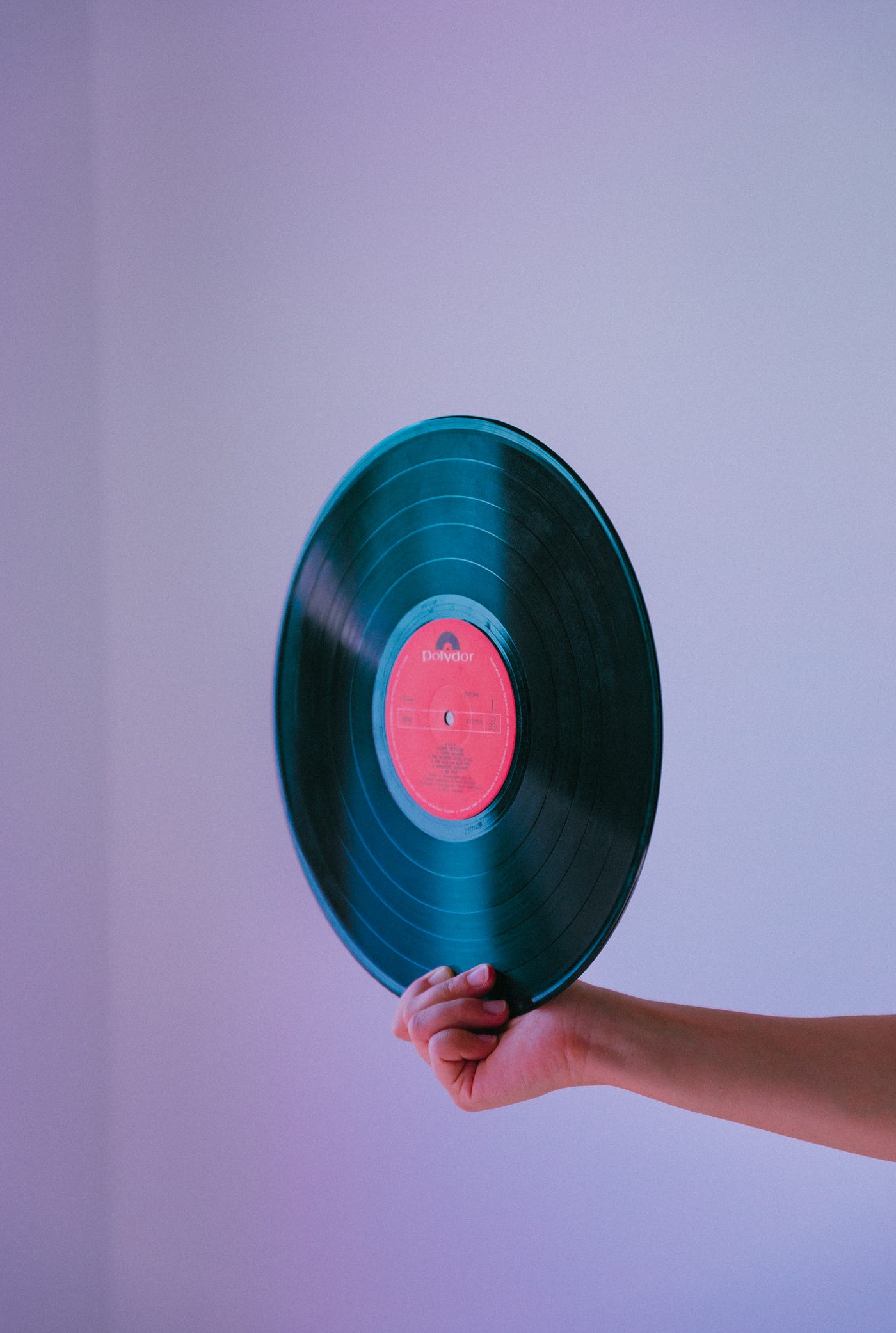 A hand extends from the right to hold an old-fashioned vinyl record (with a red center). Heart dynamics influence our momentary experience of time.