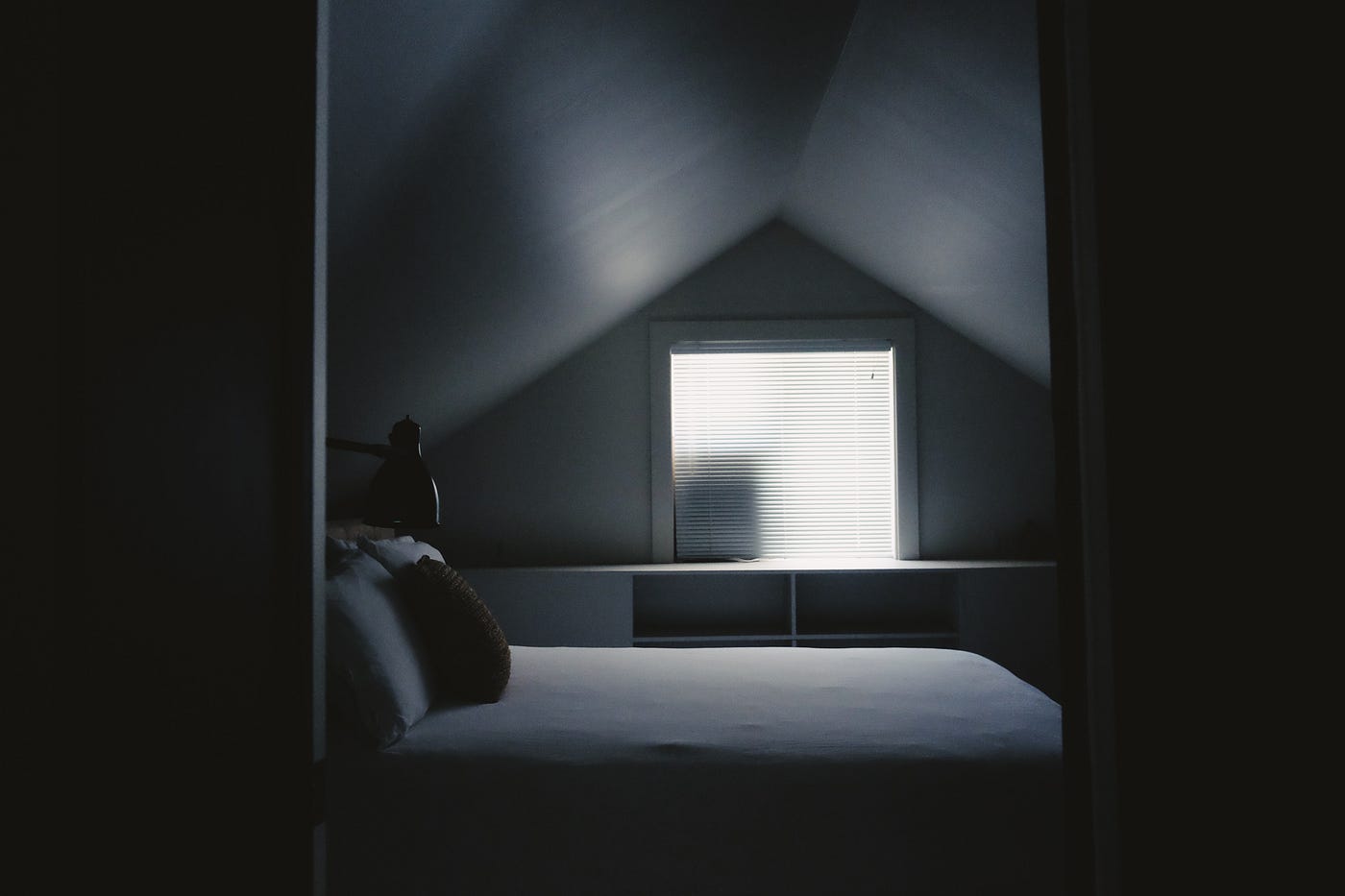 A black and white simple image of a bed in a darkened room. I am discovering this truth: With age, we sleep more lightly and get less deep sleep.