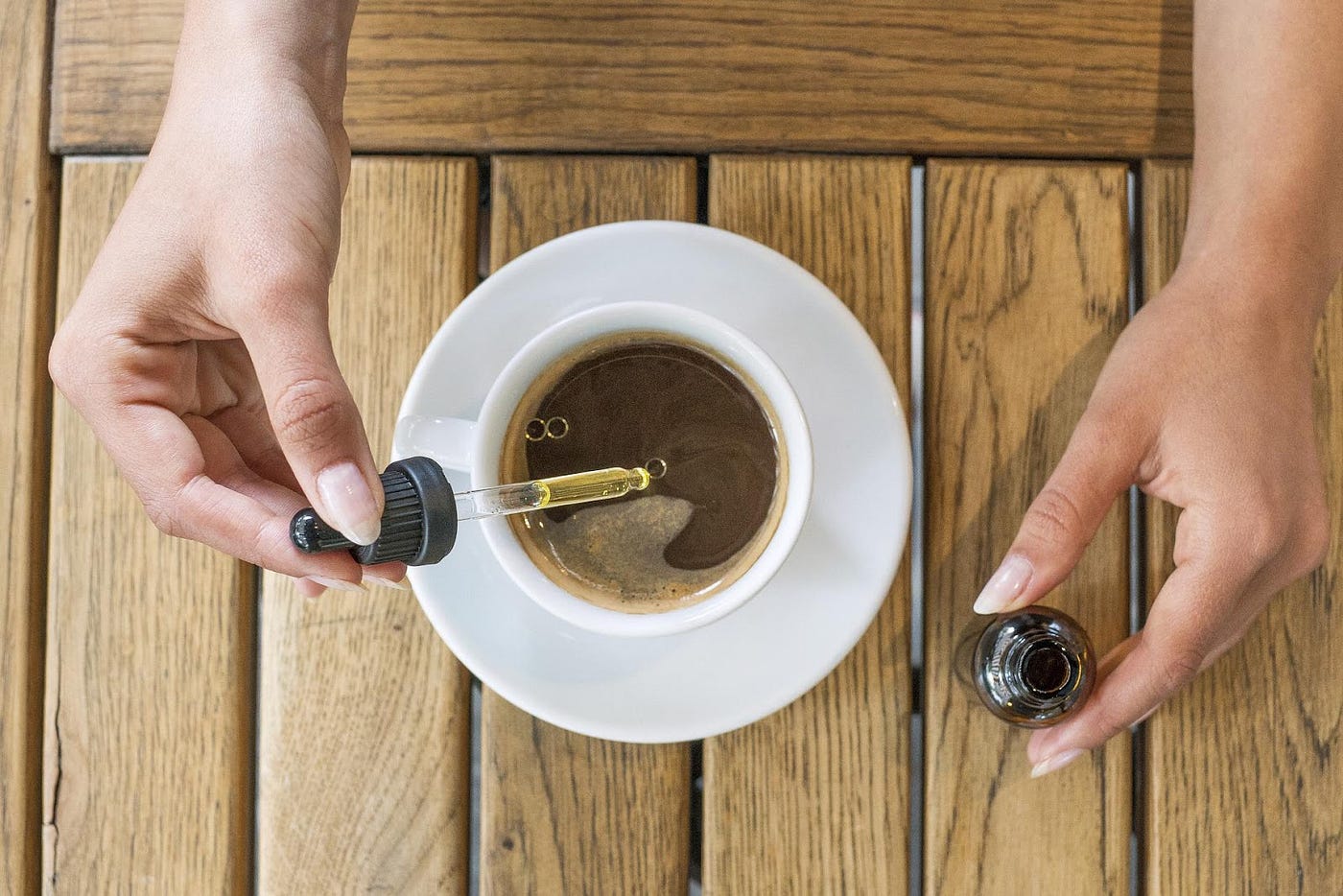 Full Extract Cannabis Oil is added with the help of a dropper from a bottle to a cup which is filled with coffee