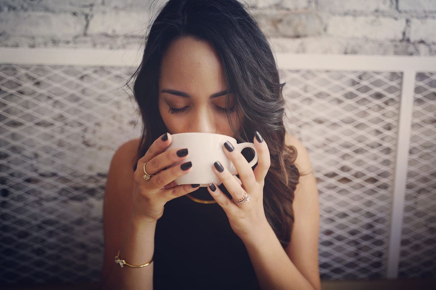 A woman with dark hair and closed eyes holding a white mug, representing the potential link between coffee consumption and the query "can coffee cause bladder infections".