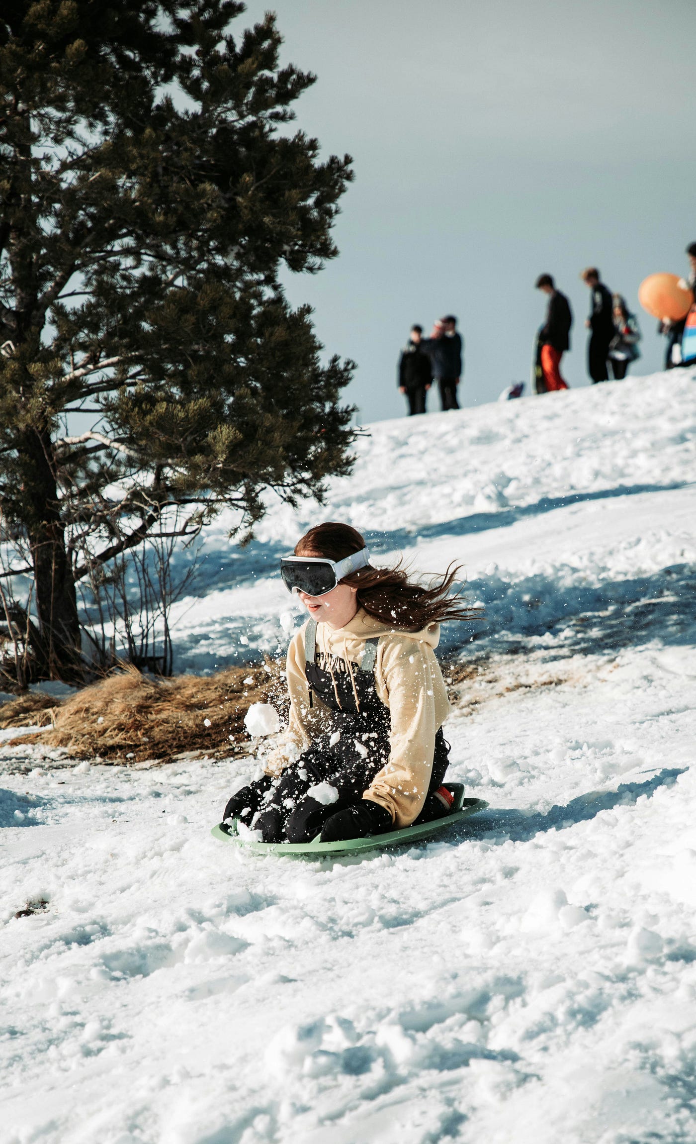 고글을 쓴 소녀가 언덕 아래로 썰매를 타고 내려갑니다.<BR>