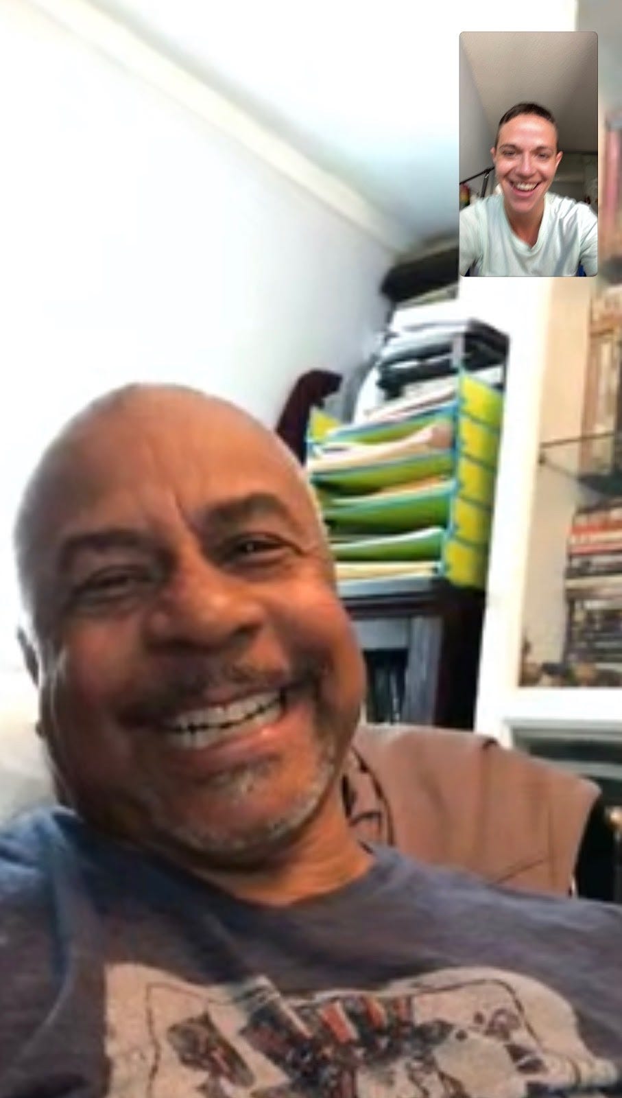 Facetime screenshot of Bobbie smiling and laughing with books in the background; Daniel’s also smiling in the upper corner.