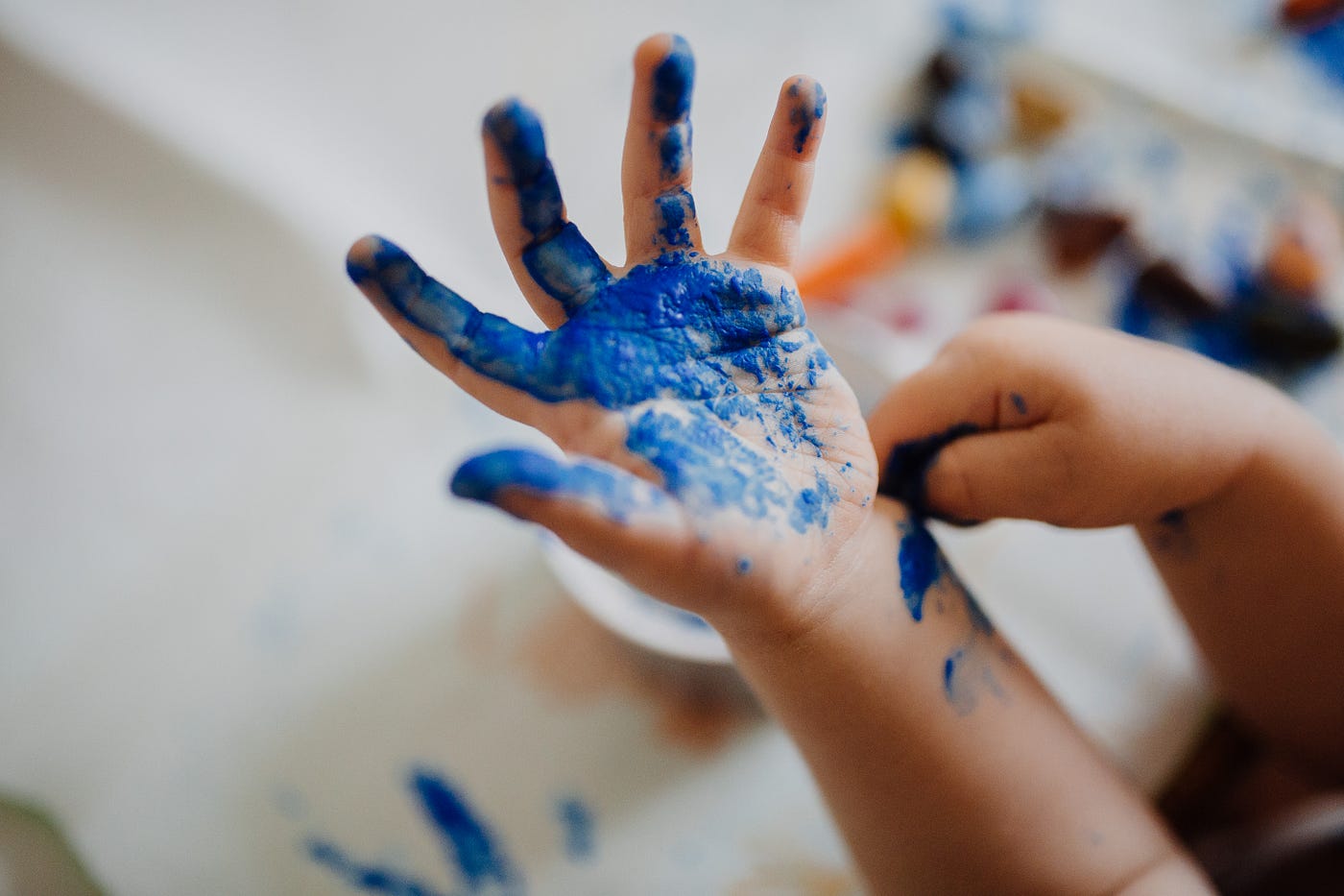 A child’s hand (covered with fresh blue paint) emerges from the lower right corner. Trichloroethylene (TCE) can be found in some paint remover.
