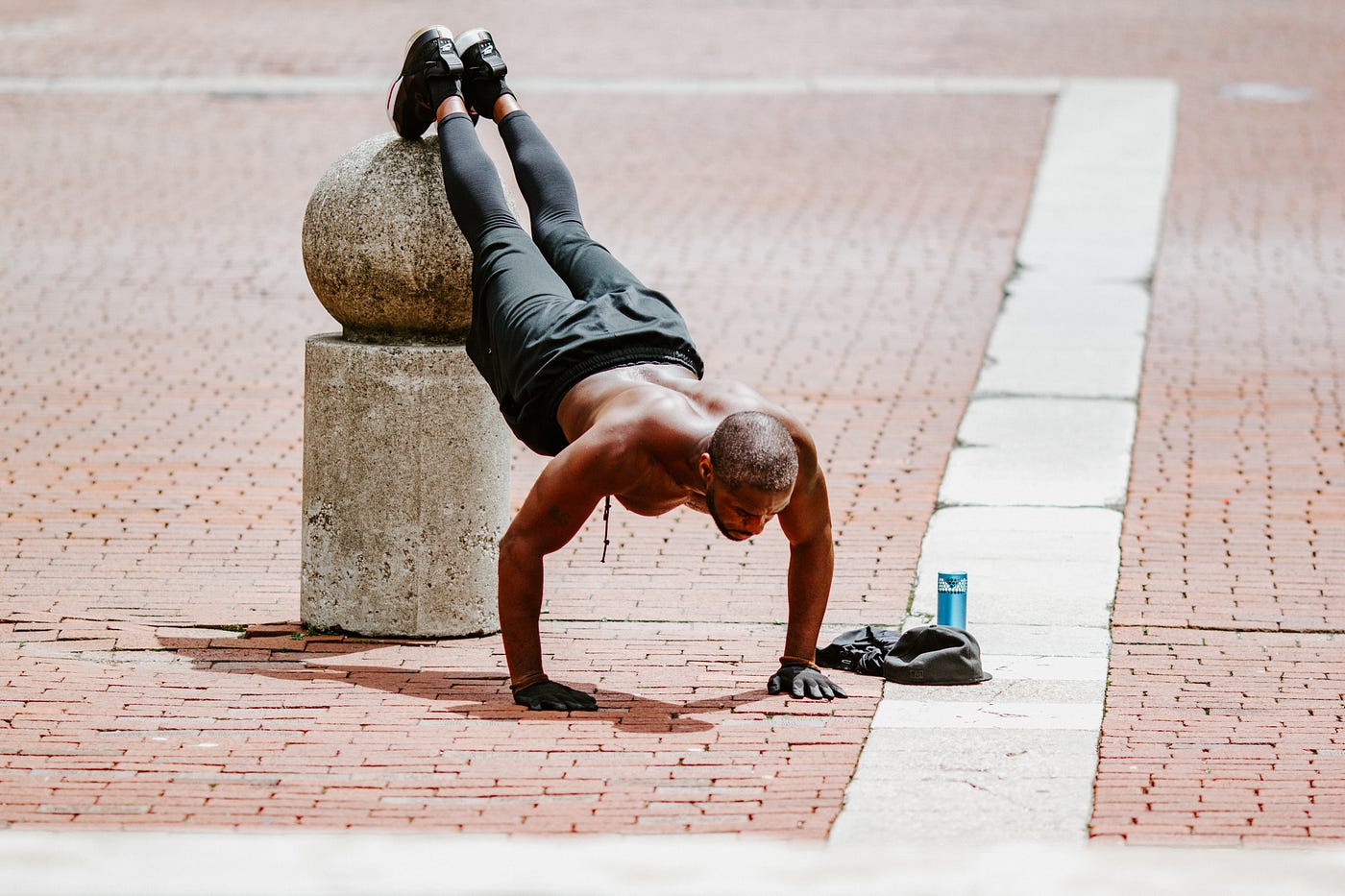 A man does decline positions, his legs elevated on a post on a brick courtyard. Compound exercises target multiple muscle groups at once, leading to muscle building and calorie burn.