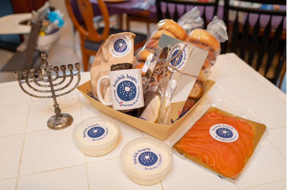Gift items with Boichik Bagels stickers on them: small wheels of cheese, a coffee mug, bagels, a menorah.