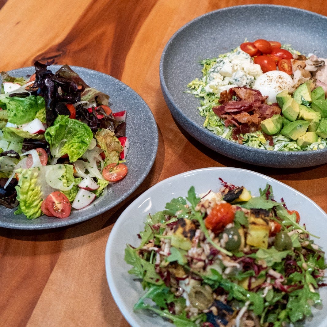 Three salads with different ingredients in bluish salad bowls on a wooden table.