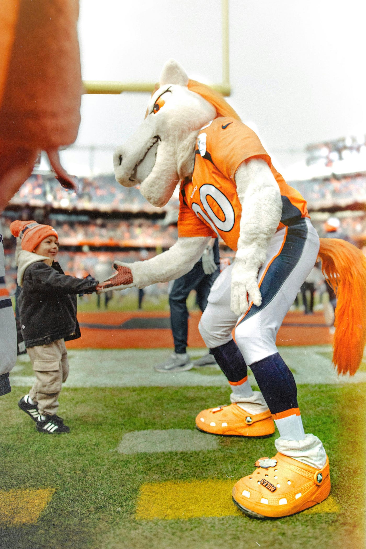 A young Denver Broncos fan shakes the hand of Denver’s mascot at Mile High in Denver, Colorado, during a past NFL season. (Photo by LOGAN WEAVER | @LGNWVR on Unsplash)