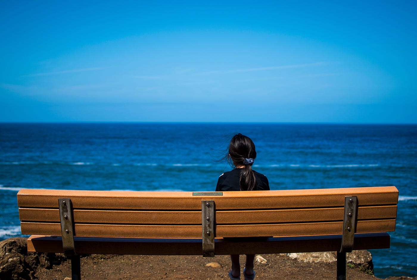 women sitting on bench facing the ocean.