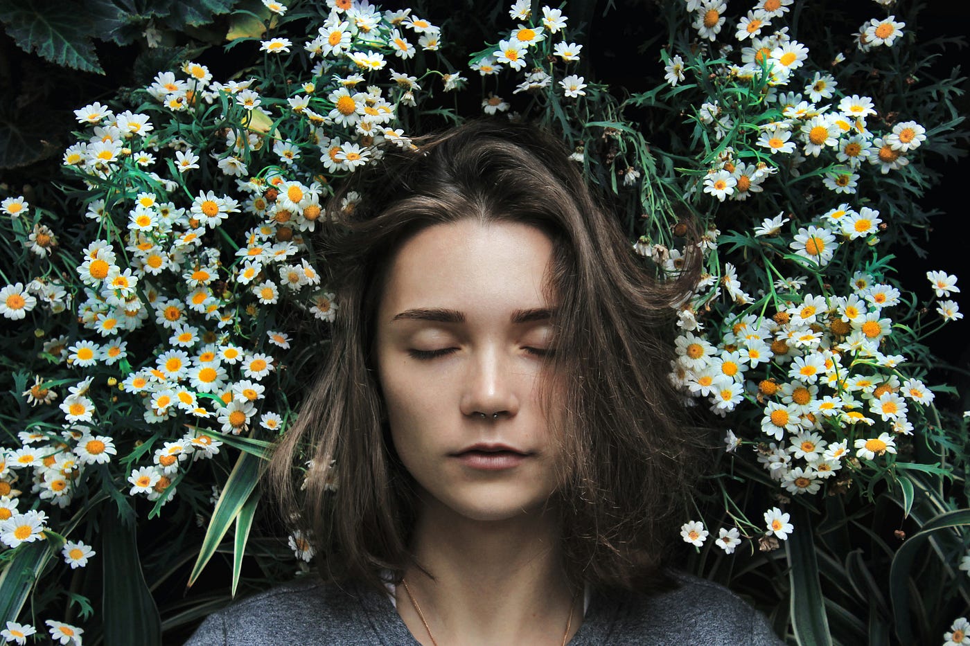 A young woman sleeps on a bed of white and yellow flowers.