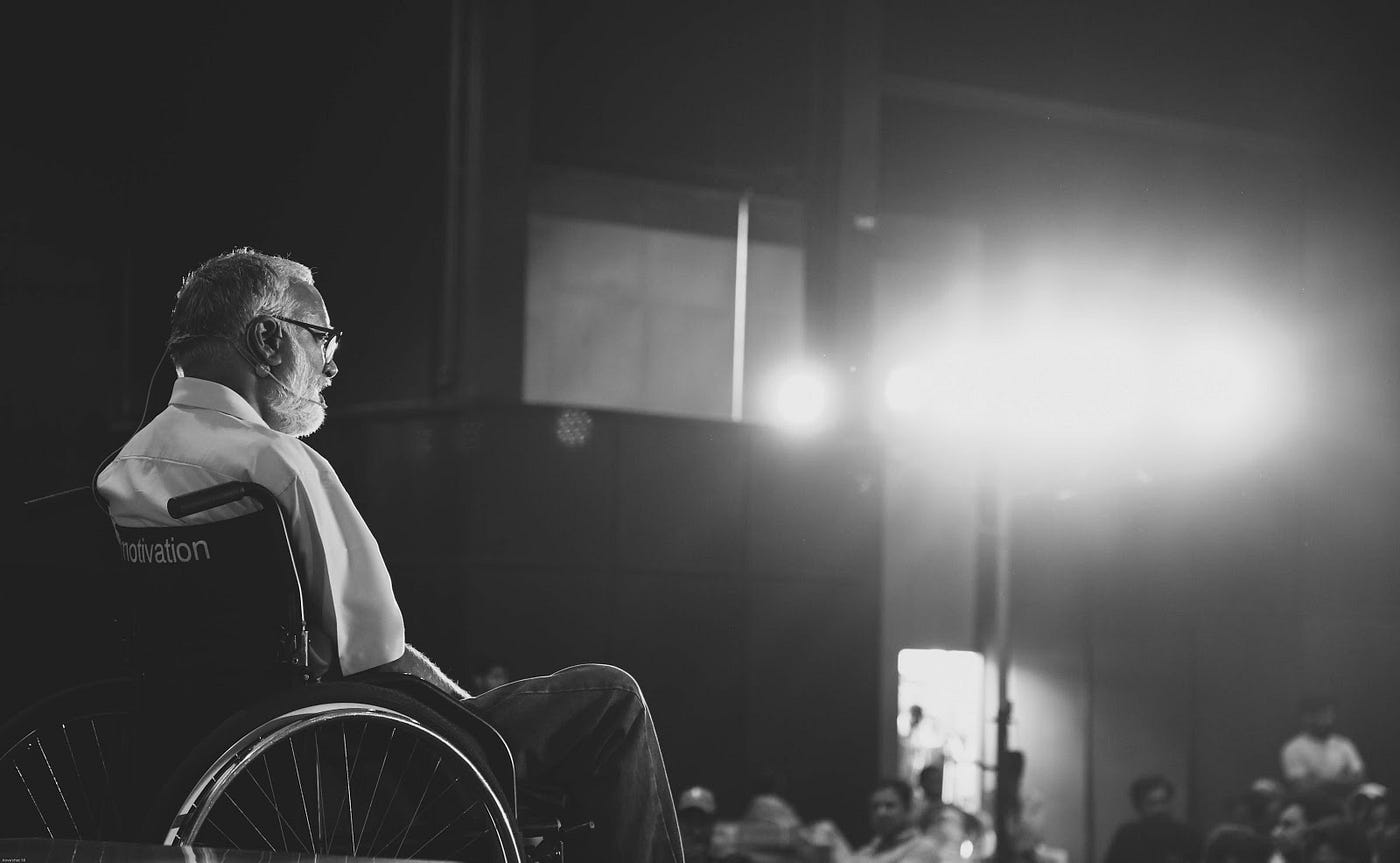 Black and white photo of Mohan Sundaram — Founding CEO & Director of Artilabs. He is in a wheelchair facing an audience.