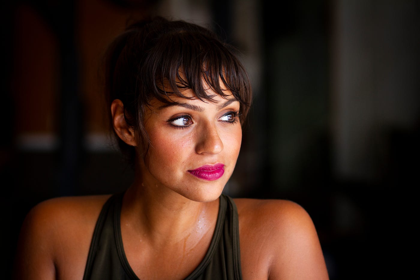 A young brunette woman looks off to her left as she faces us. She wears a tank top and we see her from upper chest up. Dark background. A​ recent systematic review and meta-analysis discovered that strength training could reduce blood pressure.