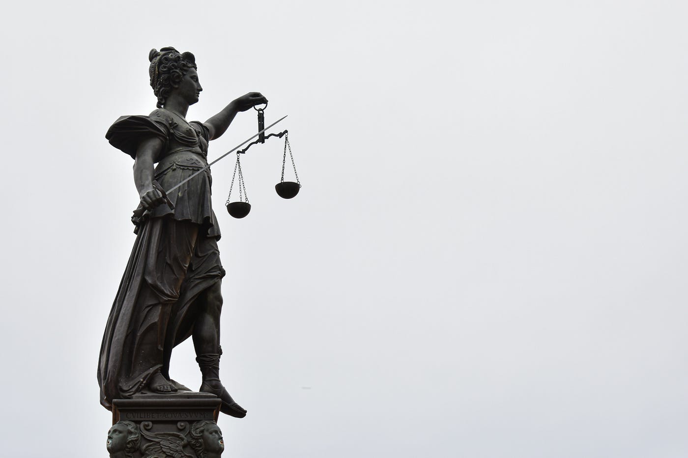 Goddess Justicia yield a sword (violence) and scales (reasoning). It can be understood both ways: either justice “cuts” with its inexorable arguments, or applies reason with one hand, and aggression with another, thereby baptising the rising Leviathanic abomination. Photo by Gaétan Marceau Caron on Unsplash