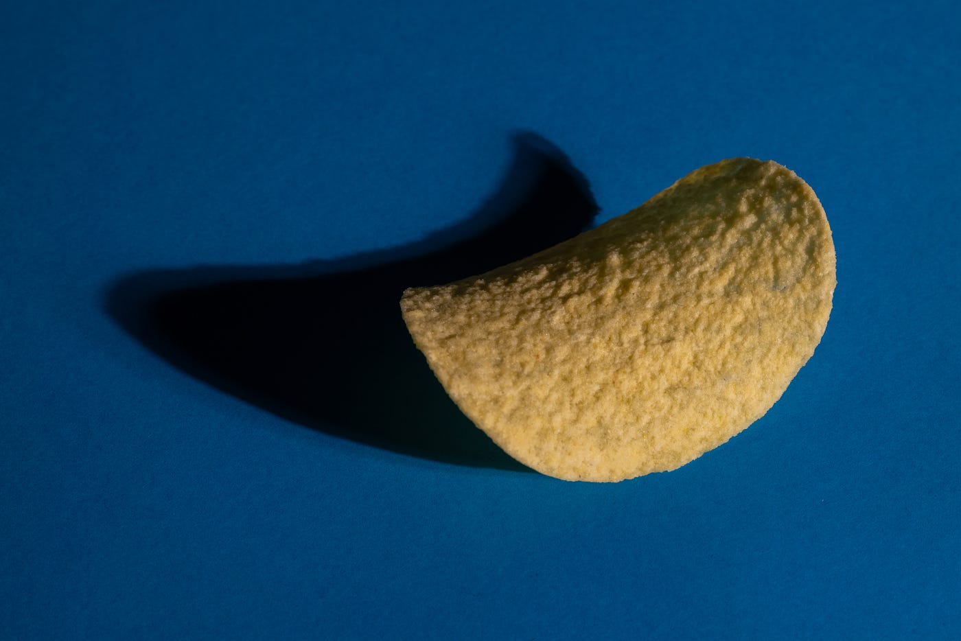 A single Pringles potato chip. Dark blue background. Ultra-processed foods are high in added sugar, oils, fats, and refined starch. These substances can impact the gut microbiome composition unfavorably. Moreover, processed foods increase weight gain and obesity risks, known risk factors for colorectal cancer.