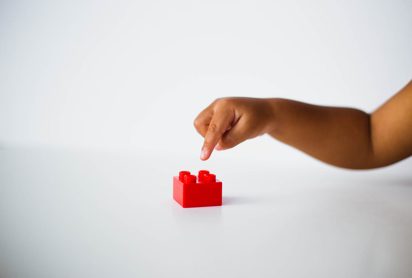 The arm of a black toddler extends from the right of the mage to almost touch a red LEGO piece. The US Centers for Disease Control (CDC) offers that individuals with an autism spectrum disorder may demonstrate restricted or repetitive behaviors or interests.