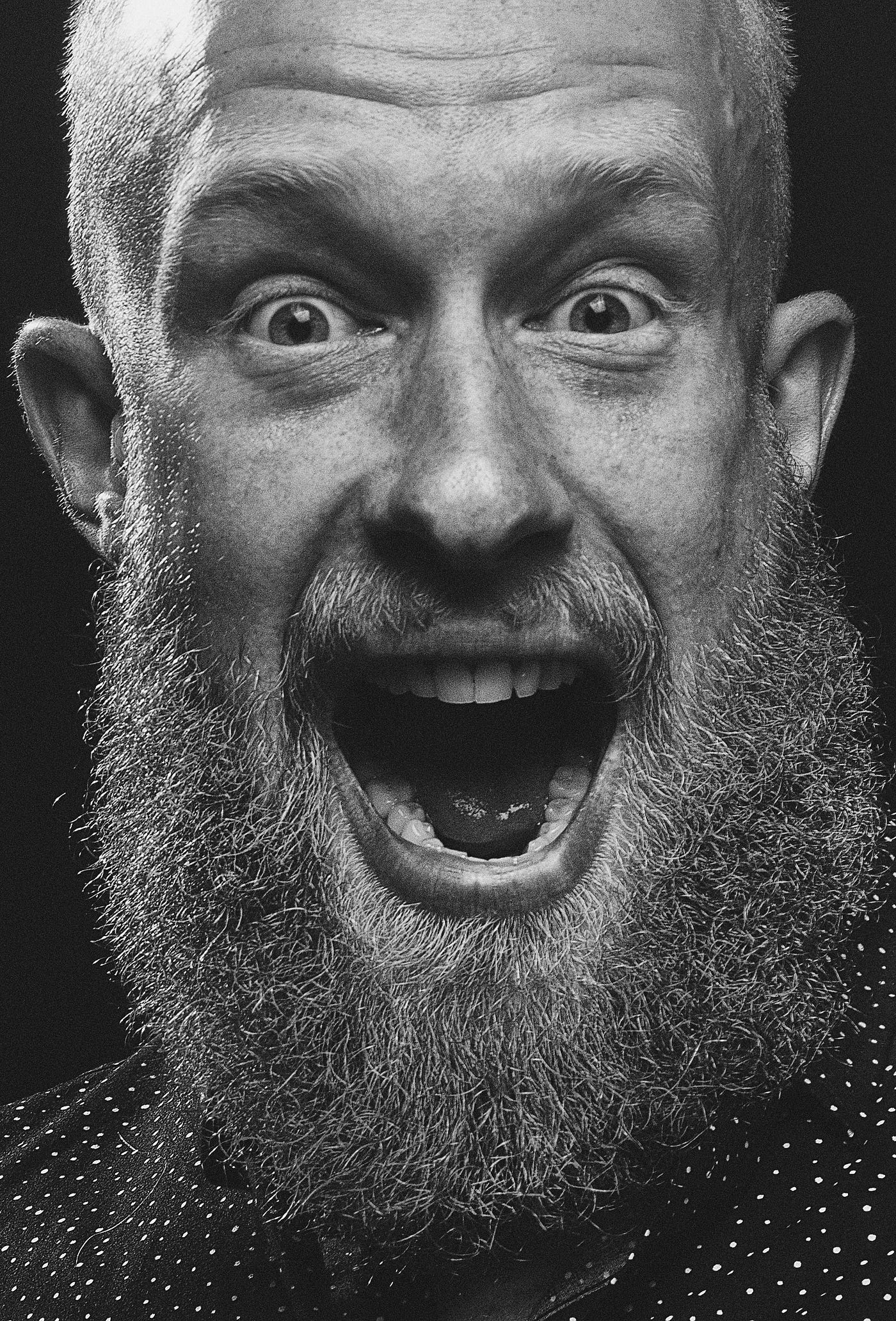 A bearded man with wide eyes and an open mouth, expressing surprise or excitement, embodies the essence of Feeling Lost in Life in a striking black and white close-up photo.