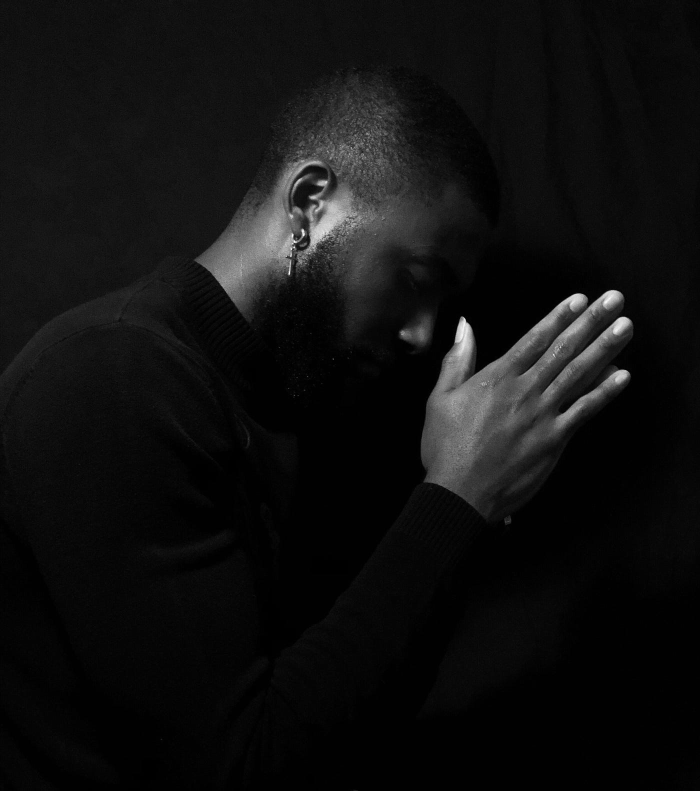 A black man is seen in profile, in black and white, as he clasps his hands in prayer.