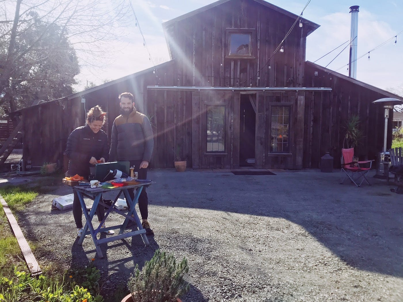 Two people standing at a small table in front of a barn.