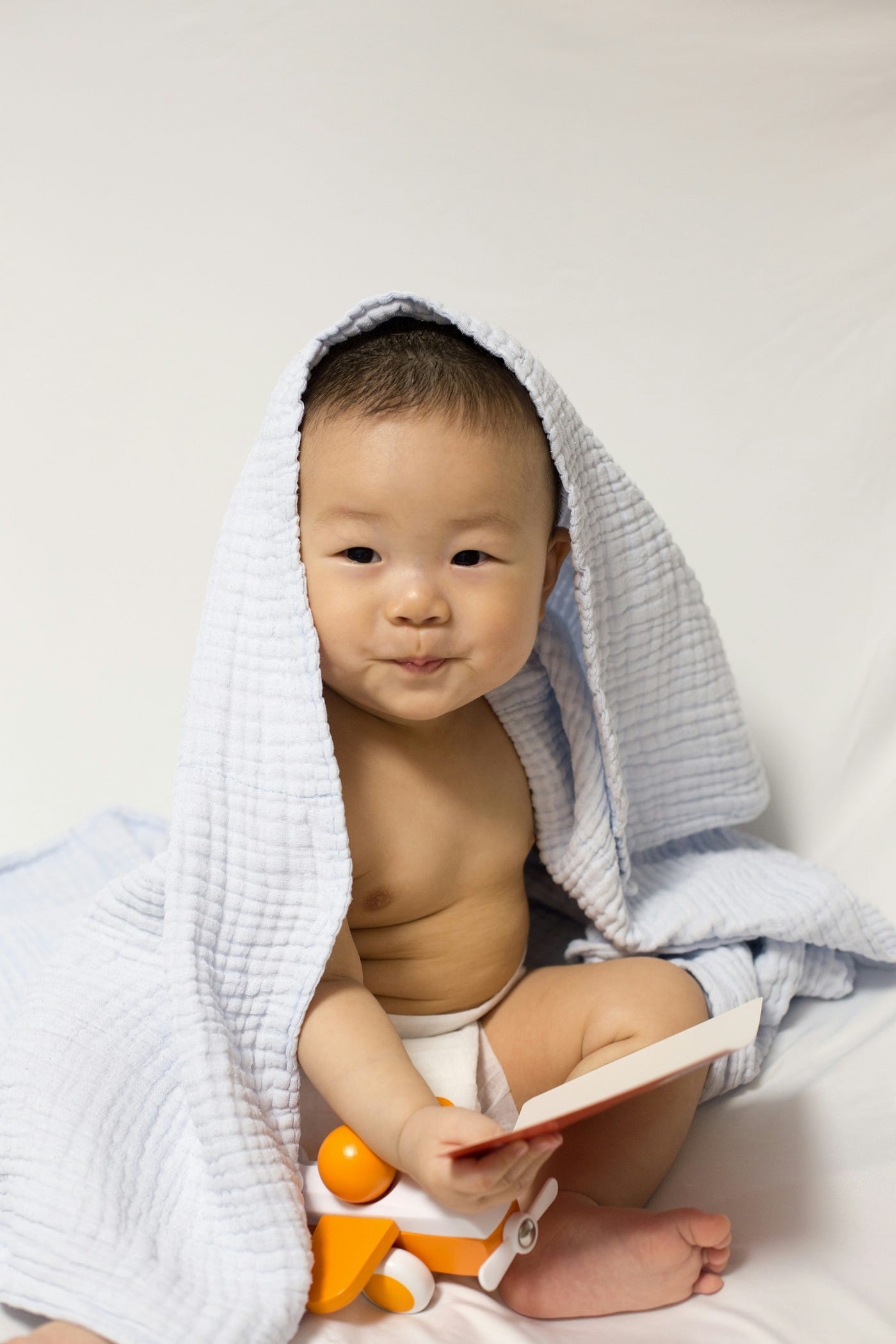 An Asian child, about one year old, sits under a blanket.