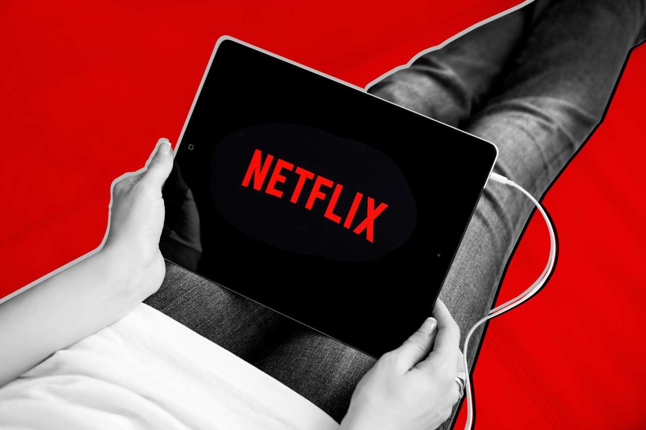 An Image showing a person holding an Ipad with Netflix logo displayed on the Screen.
