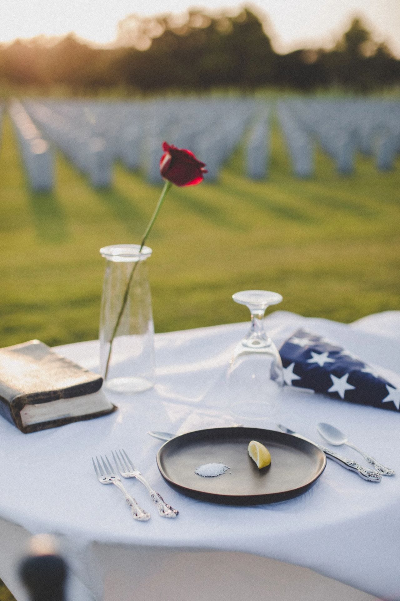 Mickey Markoff Air Sea Exec 2023 — photo of table with white tablecloth, black bible, red rose, folded American flag, black plate with white salt and lemon on plate, in front of veteran graves posted on article on gold star families