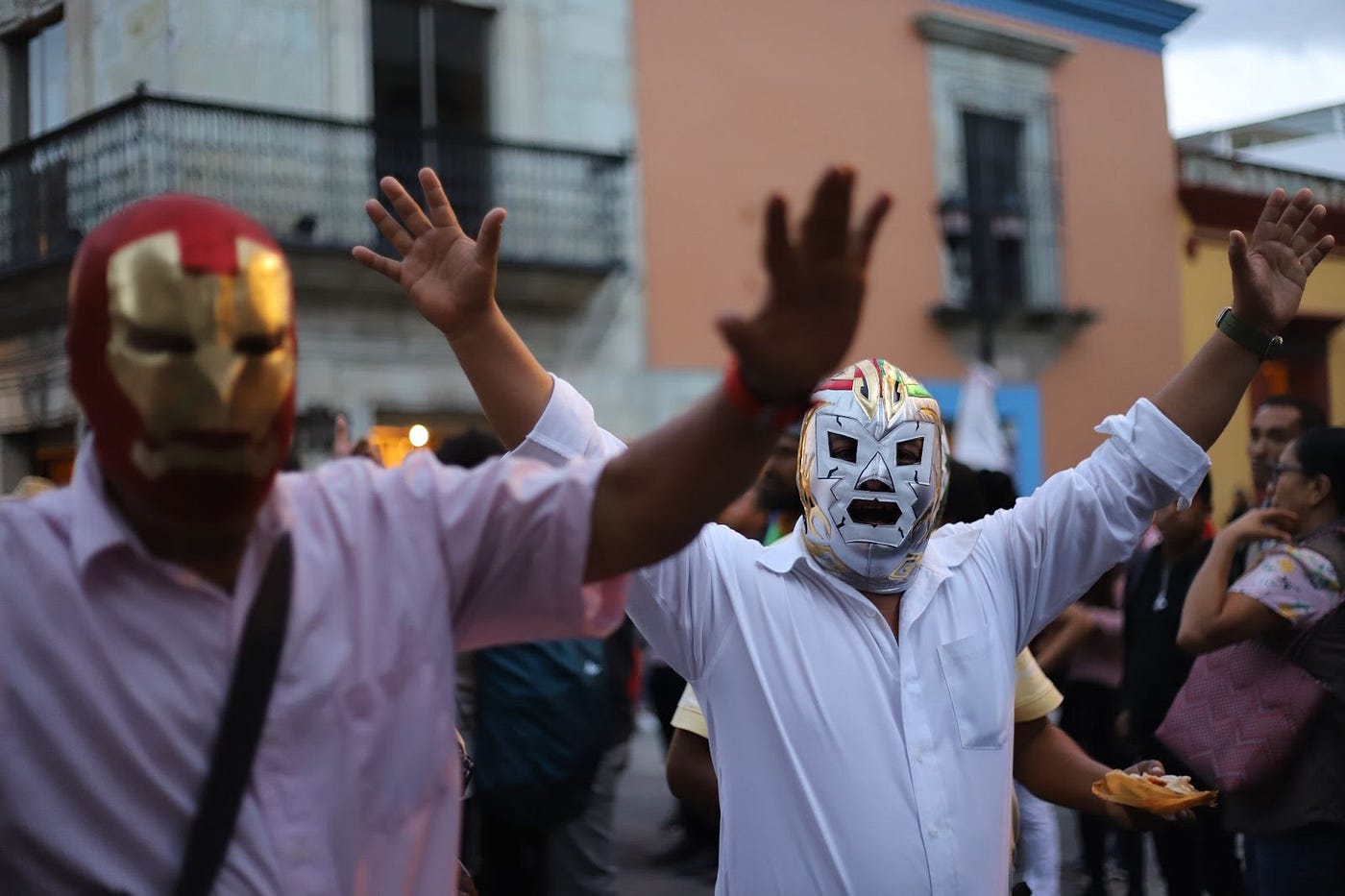 A parade with people wearing luchador masks, holding their arms aloft.