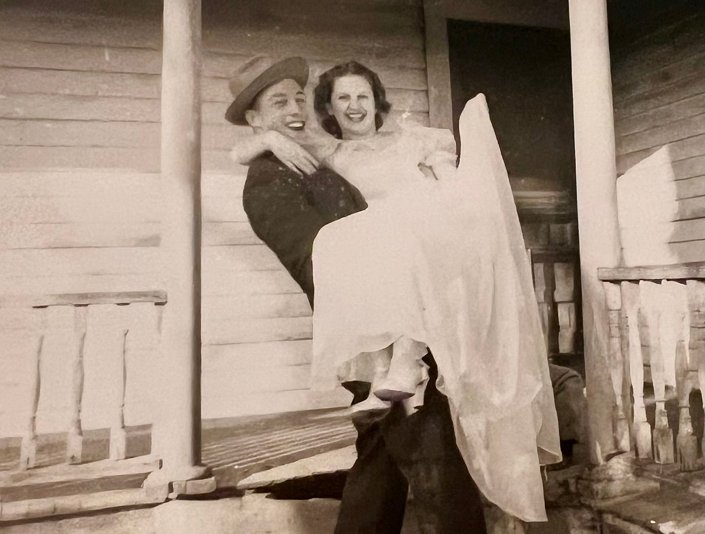 신랑이 신부를 작은 집 현관에서 안고 있는 고전적인 흑백 사진으로, 사랑과 기쁨의 순간을 포착했습니다.<BR>