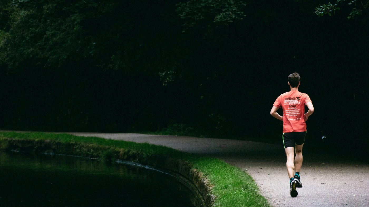 A man runs away from us, next to a man-made pond.