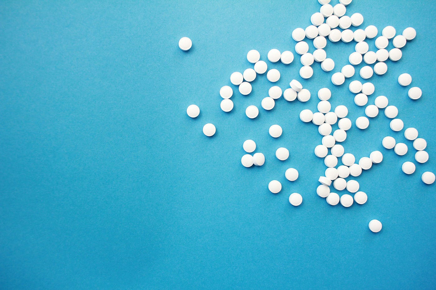Numerous small white pills, against a powder blue background.