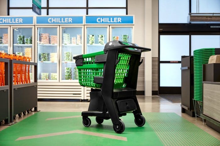 A sturdy green-and-black plastic shopping cart in the checkout lane with in front of a refrigerator case.