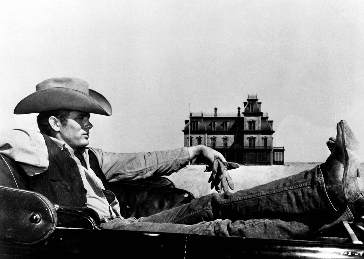 James Dean sul set de “Il Gigante” con il ranch Reata sullo sfondo, anch’esso ispirato al dipinto “Casa lungo la ferrovia” di Edward Hopper.