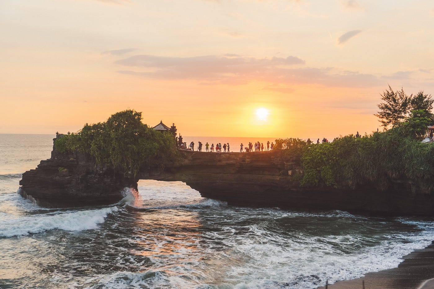 Ocean sunset at a rock formation with silhouetted people. (Photo Credit: MikeeRogers/Envato)