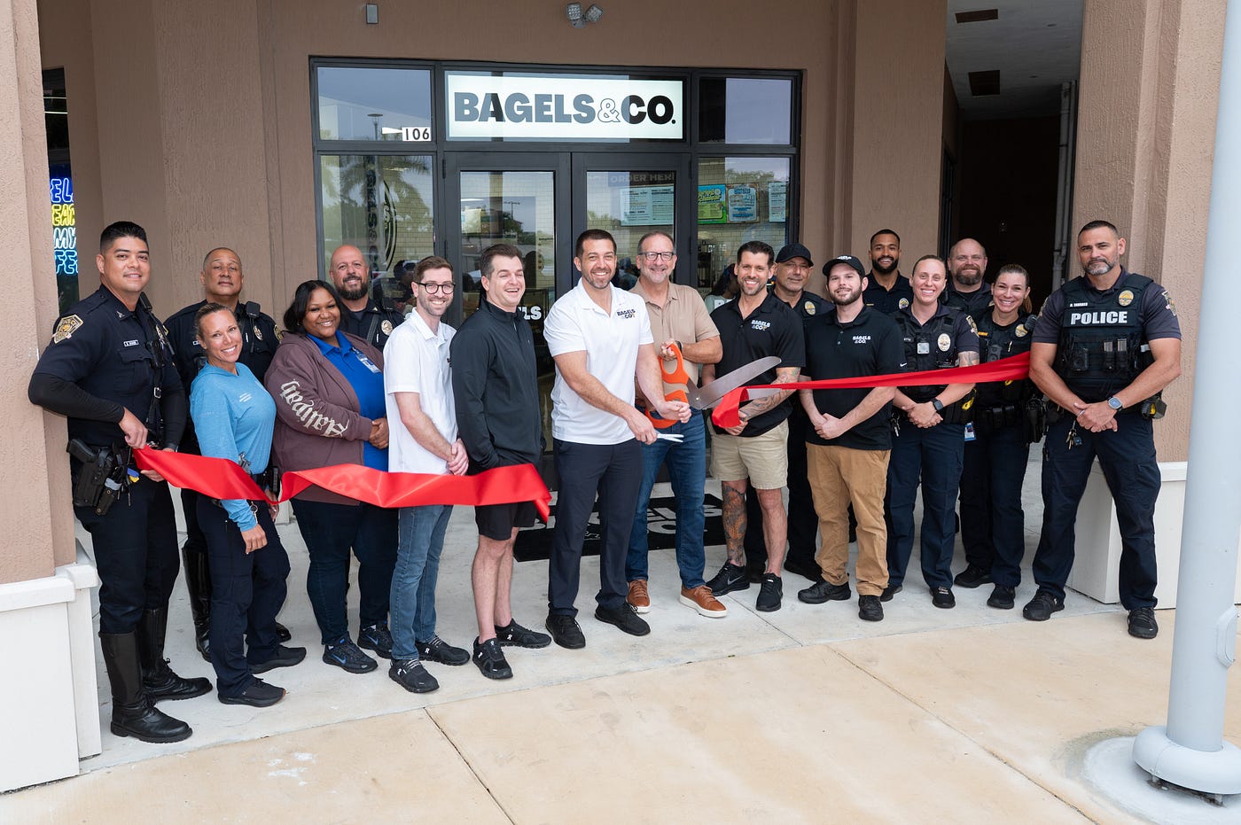 (left to right) Mark Kaplan, David Kaplan, Matthew Driscoll, Kevin Armantrout, Matthew Hoffman, Samuel Chalom and officers from the Town of Davie Police Department cut the ribbon at the Bagels & Co. in Davie. (Credit: Michael Murphy)