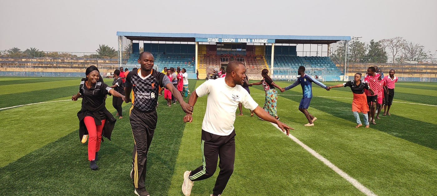 A group of people holding hands in a line and running on a green grass field.
