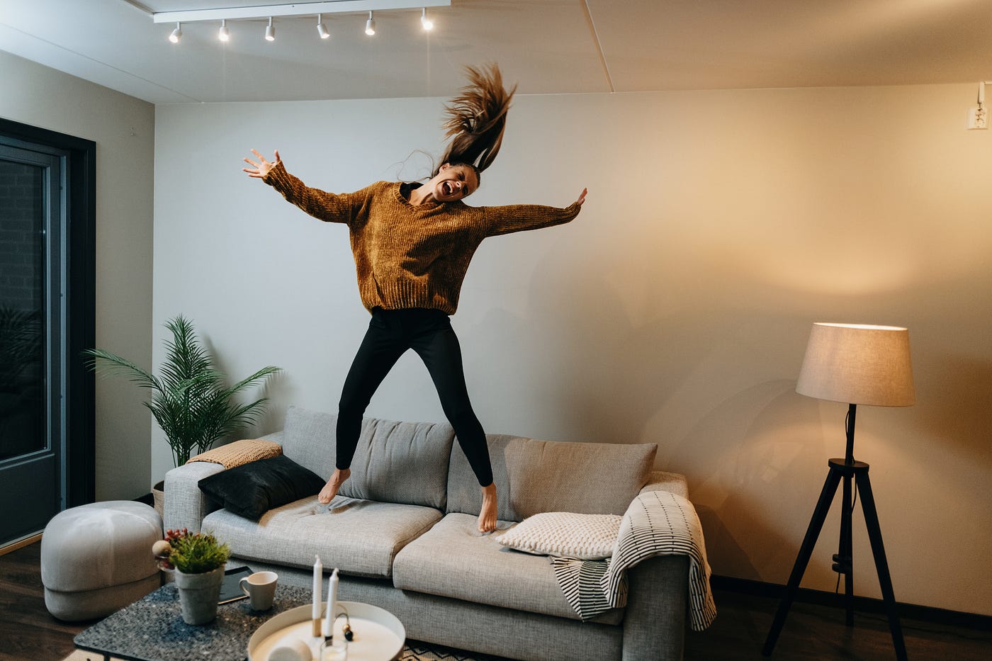 A happy woman jumping on a couch in a living room.