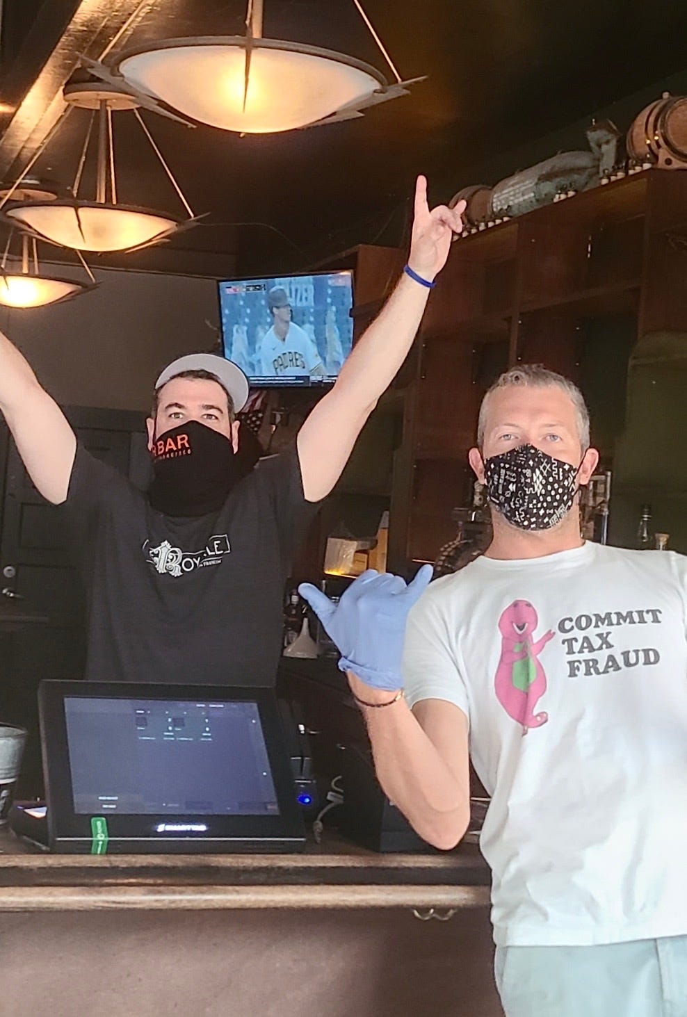 A person wearing a mask, pointing at a similarly masked DJ who has their arms up.