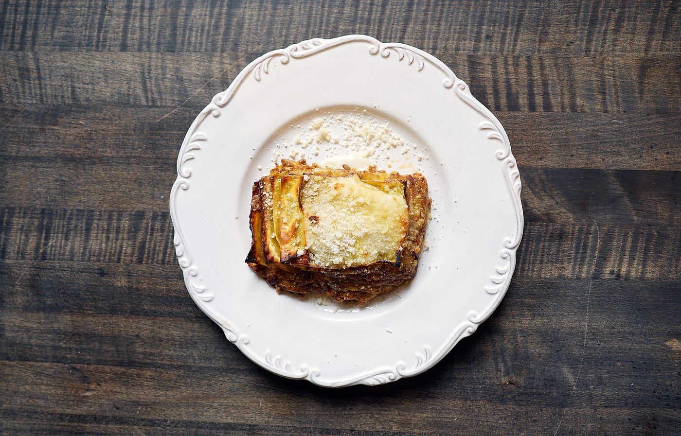 Lasagna on a white ceramic plate, on a dark-wood tabletop.