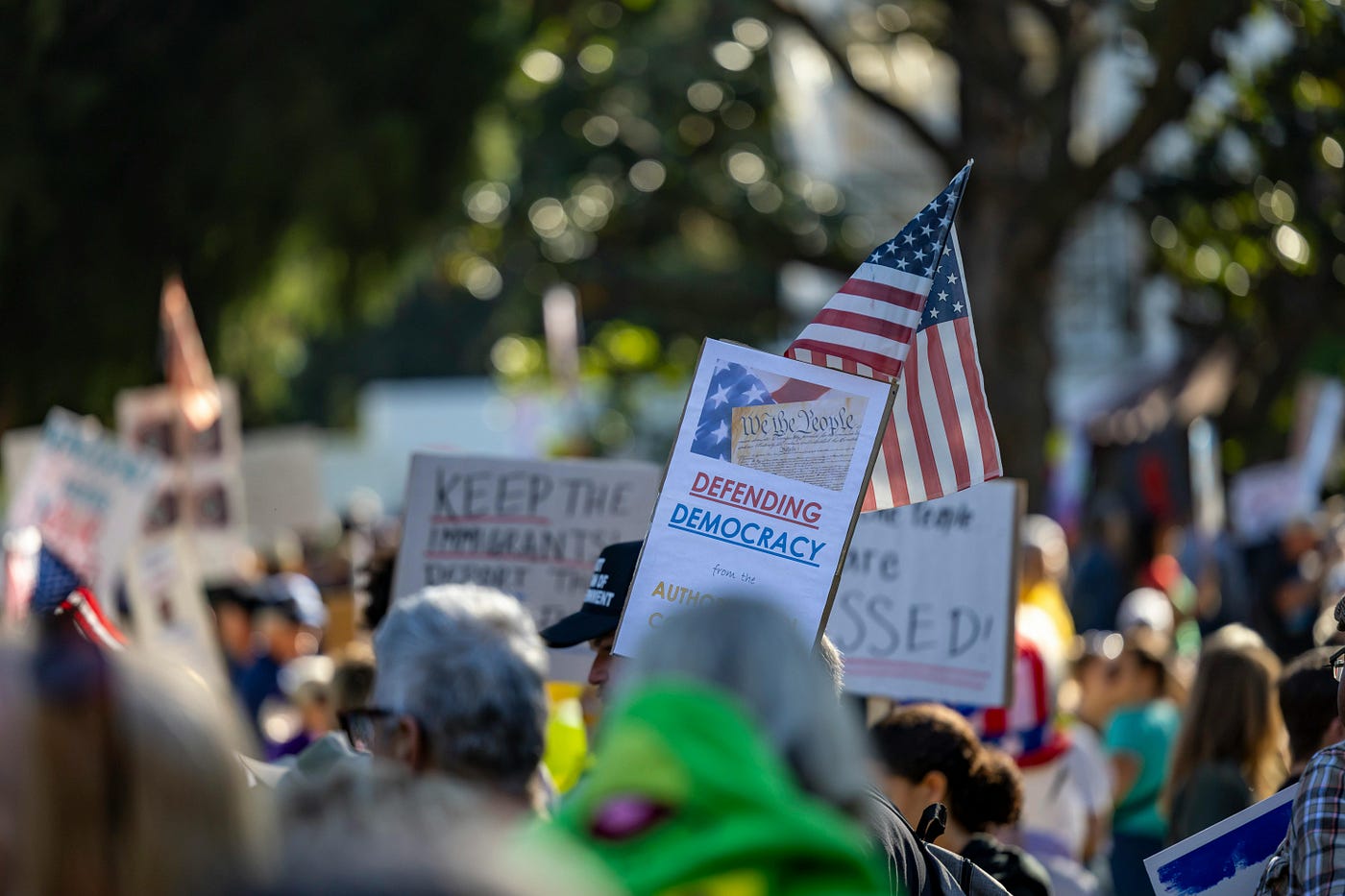 A crowd gathers in Sacramento, California to protest for defending democracy with signs and American flags.