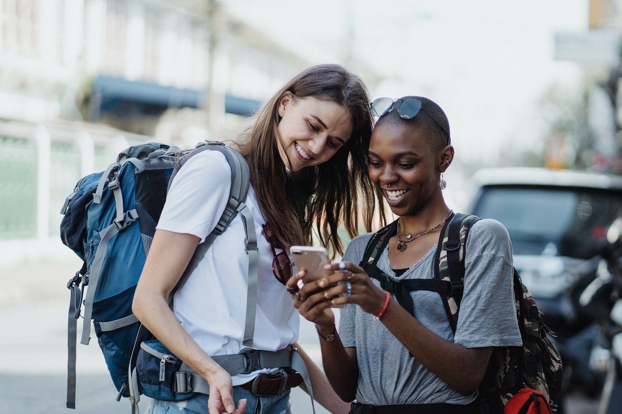 two happy travelers with backpacks, using a smartphone to explore kiwi world travel hackers' tips for affordable travel adventures. 