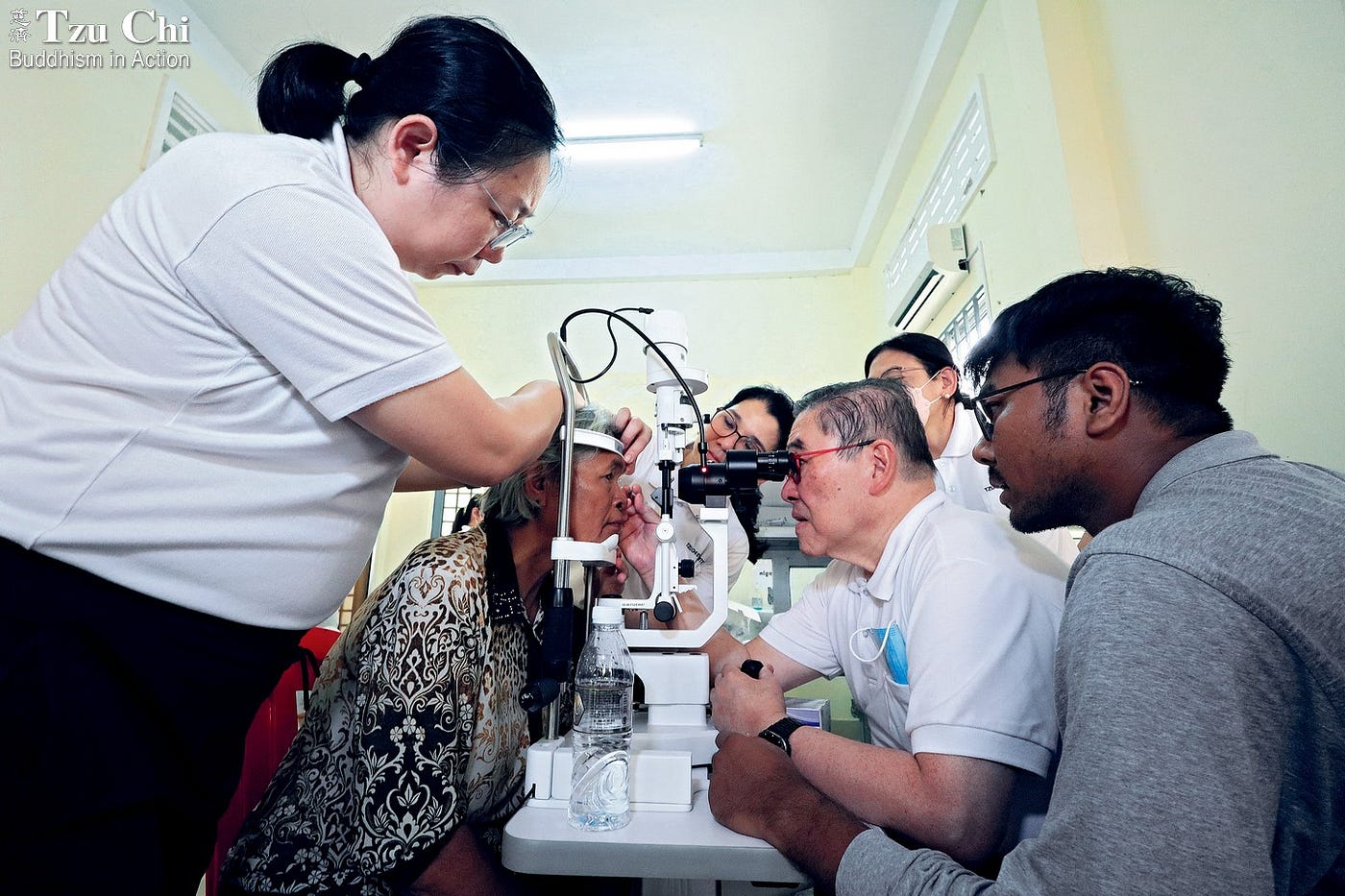 Patients in surgical gowns and caps (photo 1), with labels affixed to their foreheads, wait for cataract surgery. A volunteer applies dilating eye drops to a patient before the procedure (photo 2). Dr. Antonio Say (second from right in photo 3) from the Philippines examines a patient’s recovery the day after her surgery. (Photos 1 and 3 by Jamaica Mae Digo; photo 2 by Chai Mong Ping)