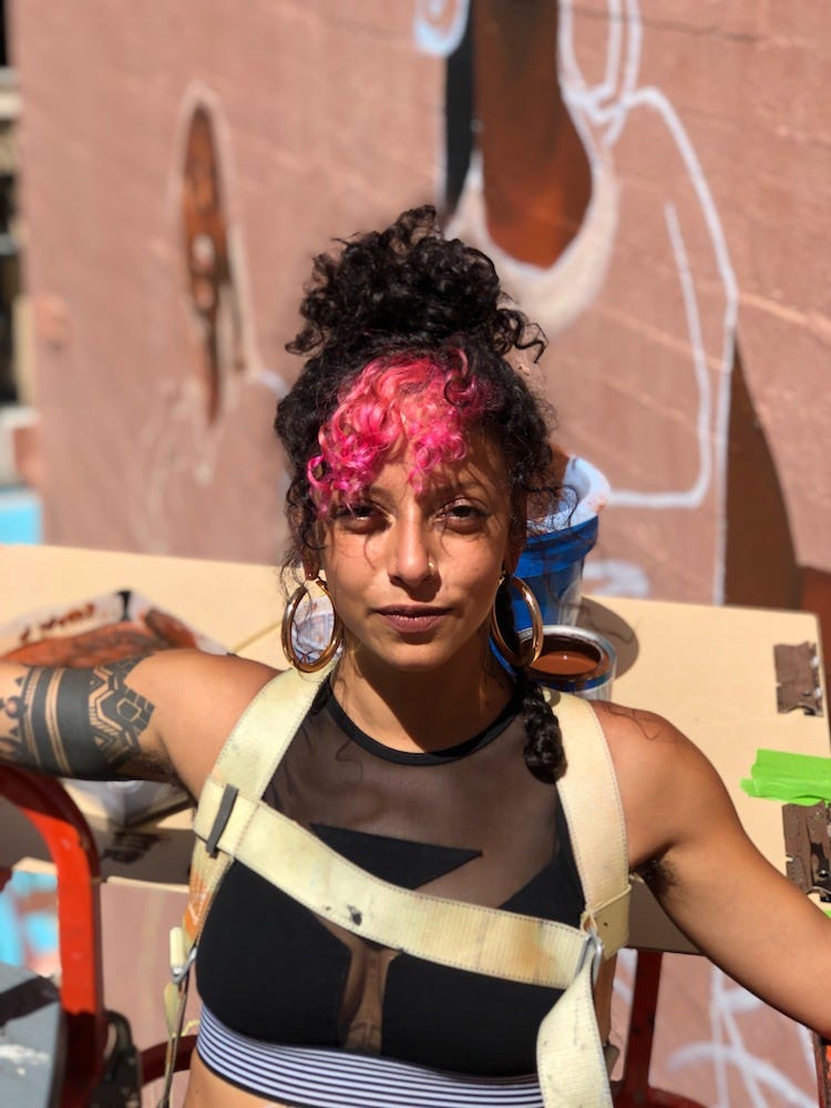 Rachel posing outdoors in front of a spraypainted wall.