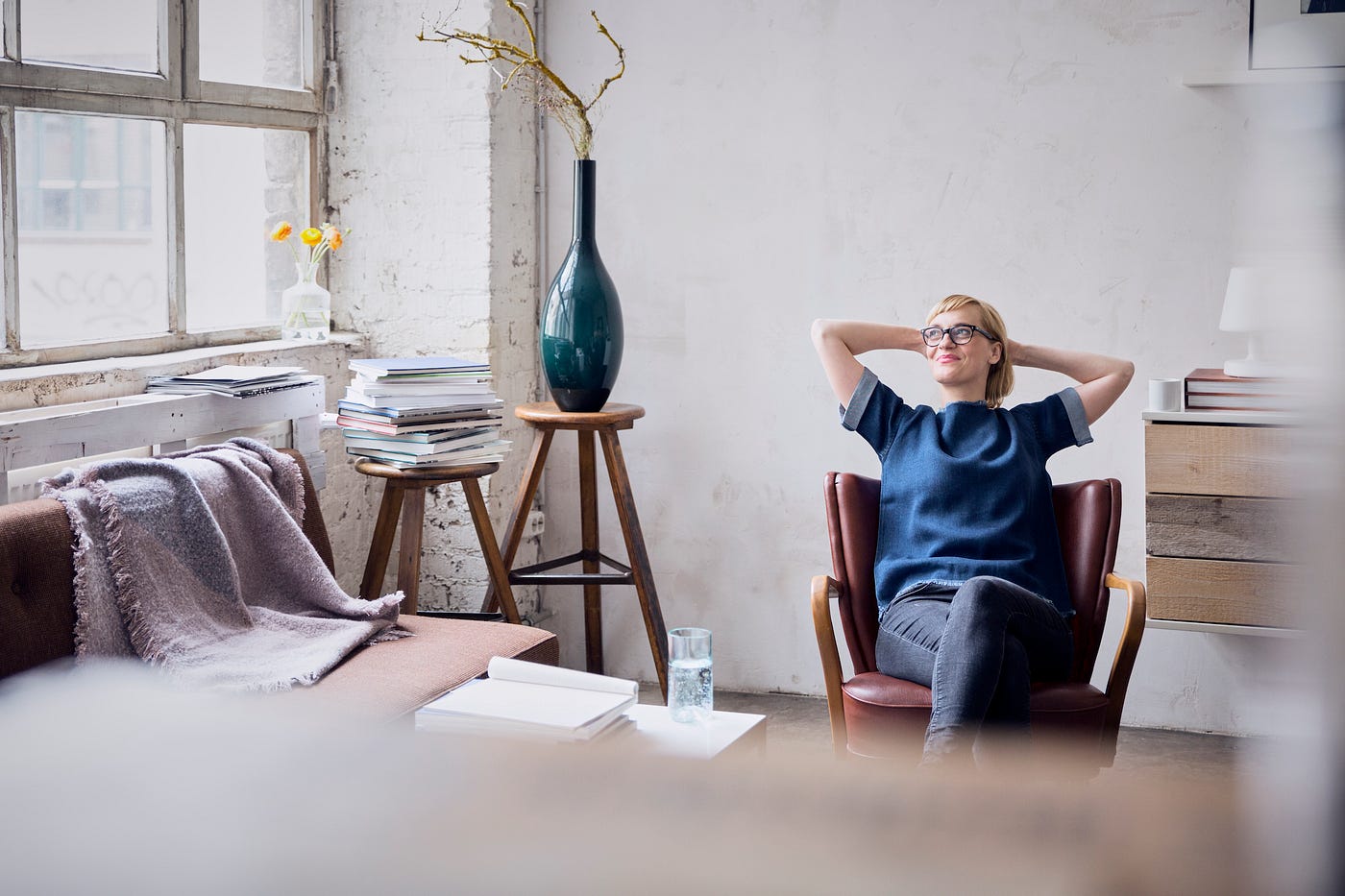 Smiling woman sitting in a desk chair in a brightly lit loft looking through a window.