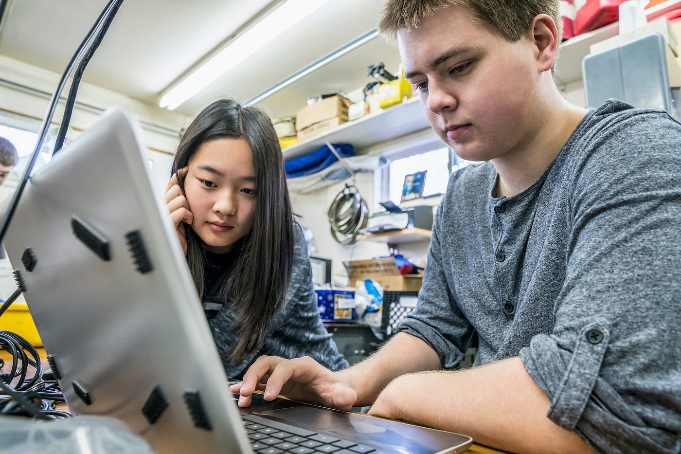 An Asian student and a white student working at a laptop in a programming lab.