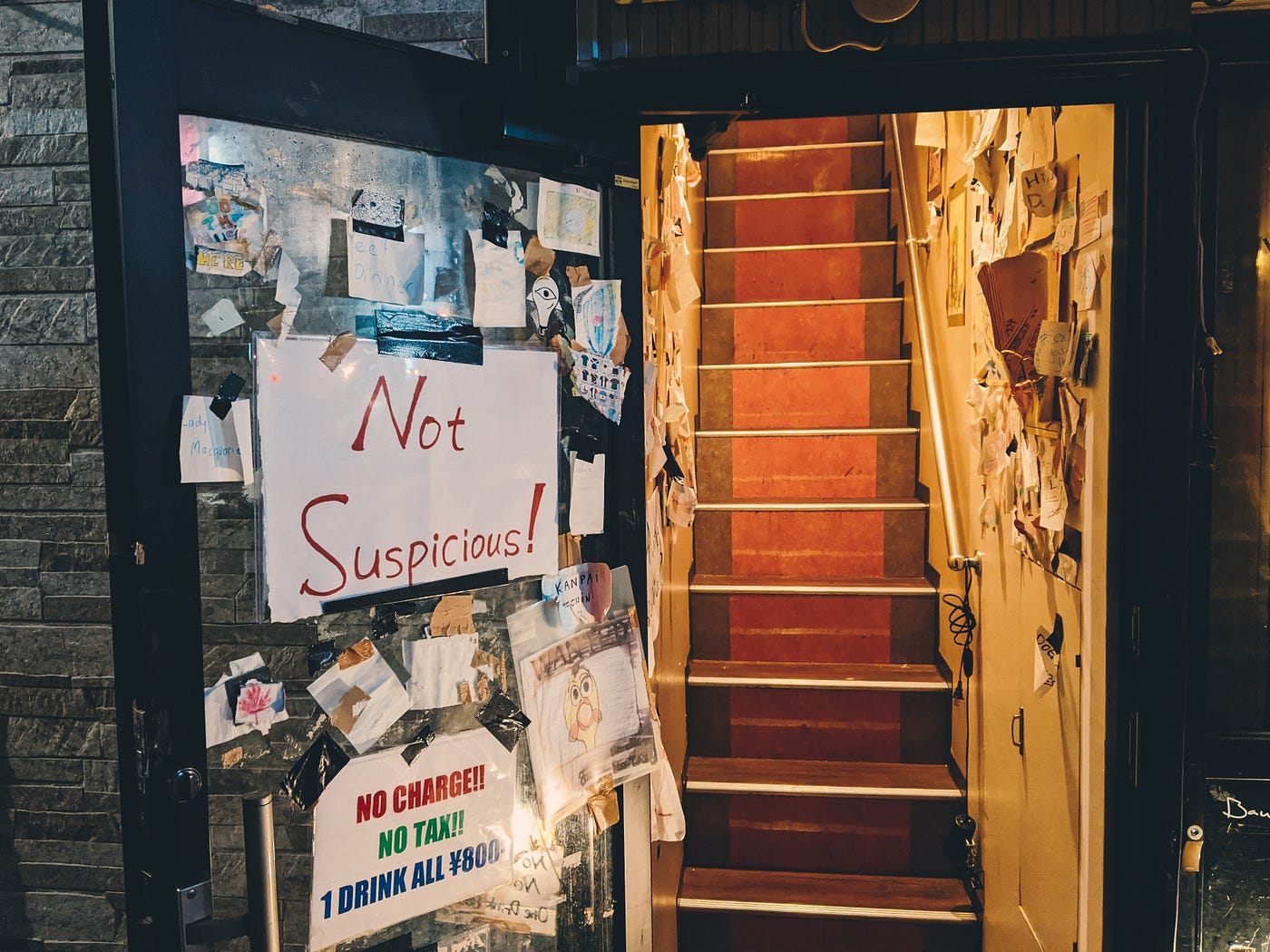 An open door to a bar with signs that say “not suspicious” and “no cover”
